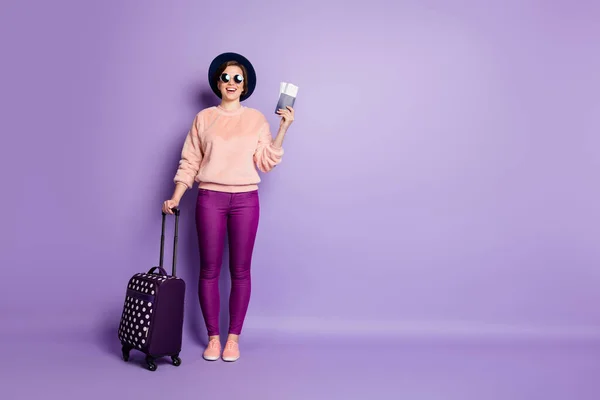 Full length φωτογραφία του αστεία κυρία διακοπές αναμονή εγγραφή πτήση κρατήσει εισιτήριο τσάντα διαβατήριο φορούν καπέλο ήλιο specs casual μοντέρνα ροζ πουλόβερ παντελόνι απομονωμένο πορφυρό φόντο χρώμα — Φωτογραφία Αρχείου