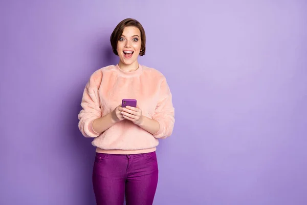 Foto di divertente blogger signora bocca aperta tenendo le mani del telefono leggere interessante idea creativa indossare casual elegante rosa pullover pantaloni isolato colore viola sfondo — Foto Stock