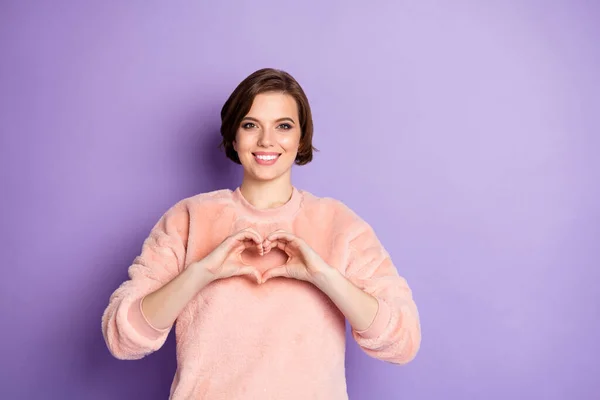 Foto de increíble joven dama haciendo manos figura del corazón sosteniendo cerca del pecho simbolizando sentimientos sinceros desgaste casual elegante suéter rosa aislado color púrpura fondo —  Fotos de Stock