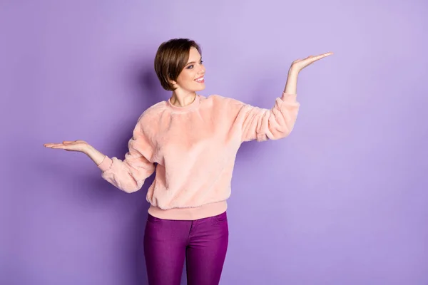 Portrait of cheerful positive girl hold hand raise palm up compare offer try choose promotion adverts wear pastel pullover isolated over violet color background — 스톡 사진
