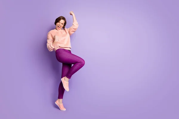 Full length photo of cheerful delighted girl celebrate her lottery lucky win raise fists shout yeah wear casual style fluffy outfit isolated over purple color background — Stock Fotó