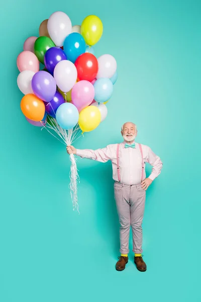 Full size photo of positive cheerful old modern man hold many helium air balls balloons enjoy festive occasion wear good look pants footwear isolated over turquoise color background — Stockfoto