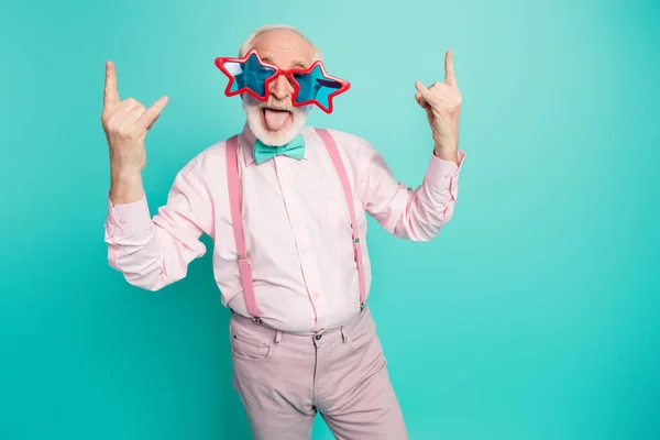 Portrait funky crazy retired gentleman make horned symbol enjoy heavy metal concert show tongue out have vintage blue starred specs wear pink grey pants isolated turquoise color background — Stockfoto