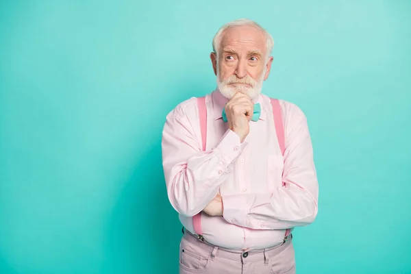 Photo de sérieux élégant grand-père tenir le bras sur le menton regarder côté espace vide profondément esprit porter pantalons chemise rose noeud papillon pantalon isolé lumineux fond de couleur sarcelle — Photo