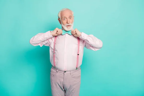 Фото смешной стильный взгляд дедушка держит руки застегивая галстук хороший веселый настроение носить розовые подтяжки рубашки бабочка галстук брюки изолированы яркий бирюзовый цвет фона — стоковое фото