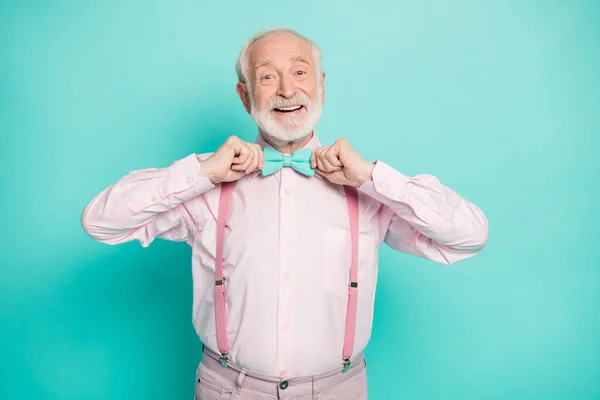 Photo of funny stylish look grandpa hold hands buttoning necktie positive emotions wear pink shirt suspenders bow tie pants isolated bright teal color background