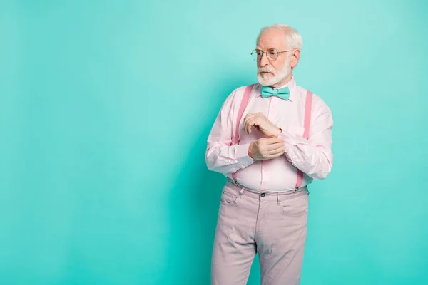 Photo of attractive serious hipster grandpa preparing senior meeting party buttoning sleeve look empty space wear specs pink shirt suspenders bow tie pants isolated teal color background — 스톡 사진