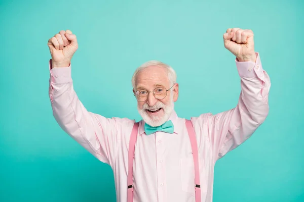 Closeup photo of attractive crazy excited grandpa raise fists up celebrating money income wear specs pink shirt suspenders bow tie isolated teal color background