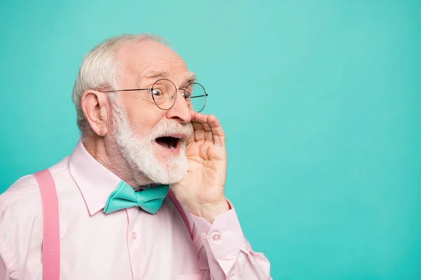 Closeup profile photo of attractive grandpa screaming side empty space hand near mouth share secret information wear specs pink shirt suspenders bow tie isolated teal color background — Stok fotoğraf