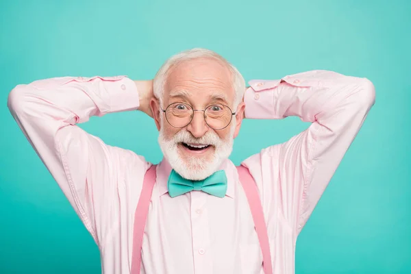 Closeup photo of funny grandpa positive cheerful facial expression good mood arms behind head wear specs stylish pink shirt suspenders bow tie isolated teal color background — Stockfoto