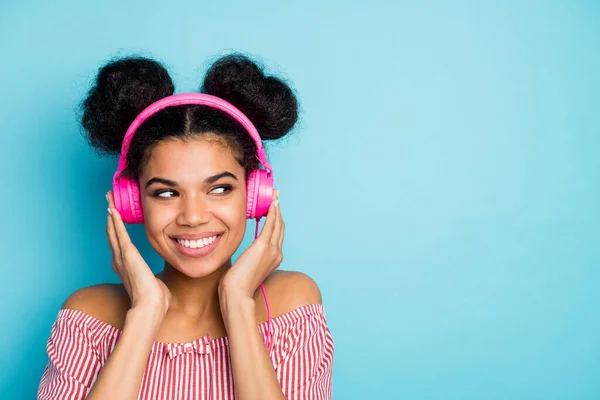 Closeup photo of funny interested dark skin lady listen music modern earphones look side empty space wear trendy red white striped shirt off-shoulders isolated blue color background