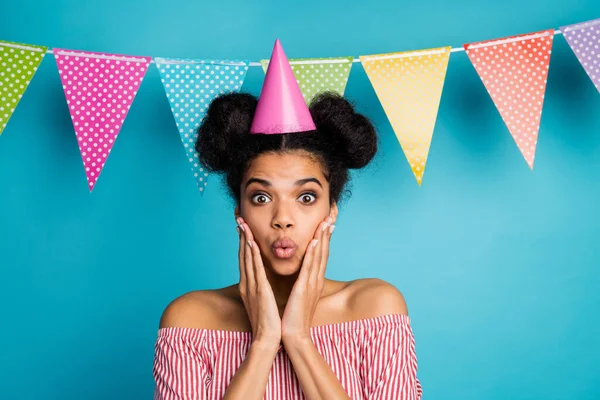 Photo of funny shocked dark skin lady arms cheekbones unexpected birthday party wear cone cap red white striped shirt naked shoulders colorful dotted flags hang over blue background — Stock fotografie