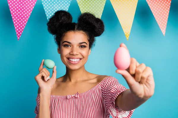 Photo of pretty dark skin lady hold holiday painted eggs colorful decor flags good mood family meeting dinner wear red white striped shirt naked shoulders isolated blue color background — Zdjęcie stockowe