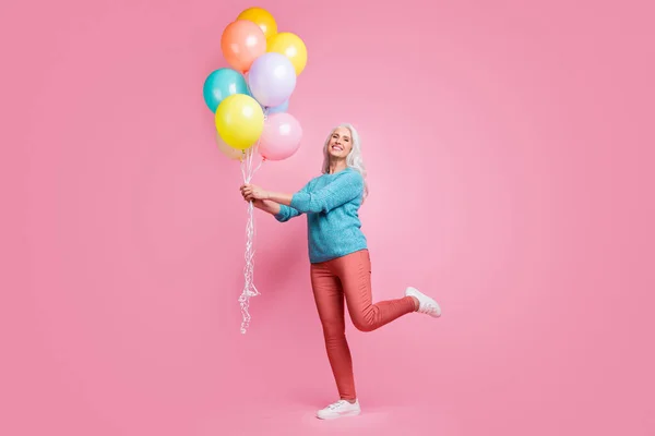 Full length photo of positive cheerful lovely pretty grandmother hold air helium baloons enjoy festive family occasion wear sweater pullover sneakers isolated pastel color background — Stockfoto