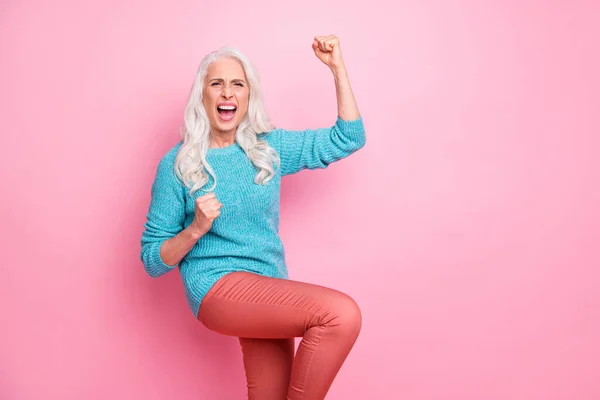 Portrait of ecstatic cheerful old woman celebrate lottery win raise fists scream yeah wear shine warm blue sweater isolated over pastel color background — Stock fotografie