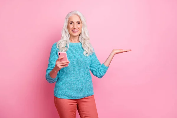 Portrait of positive cheerful old woman promoter use smartphone hold hand recommend online product ads promotion wear casual style sweater isolated over pastel color background — 图库照片
