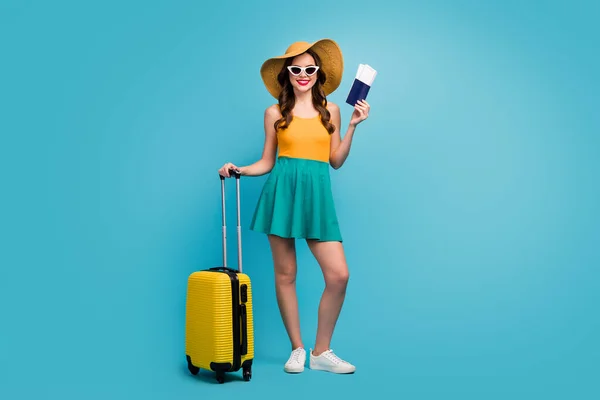 Full size photo of pretty lady traveler hold passport tickets rolling suitcase registration airport plane flight wear sun specs short summer dress headwear shoes isolated blue background — Stockfoto