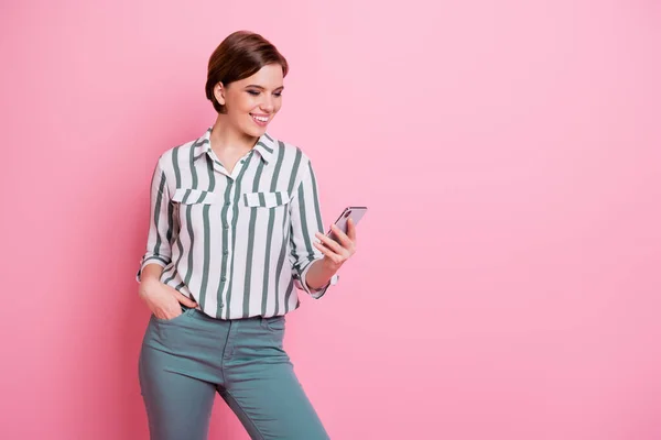 Pozitif neşeli kızın portresi akıllı telefon kullan sosyal ağ bilgilerini oku yorumları abone ol pembe renkli arka planda izole edilmiş modern giysiler giy — Stok fotoğraf
