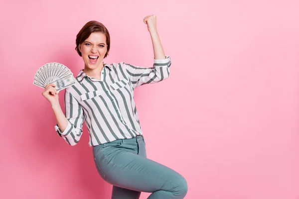 Porträtt av glada glad flicka hålla pengar fan fira kasino casback lotteri vinna höja nävar skrika ja bära grå elegant outfit isolerad över rosa färg bakgrund — Stockfoto