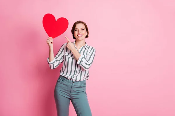 Olha o que recebo no feriado de 14 de fevereiro. positivo alegre menina data com namorado mantenha grande papel cartão coração ponto indicador dedo desgaste elegante roupas isoladas sobre cor rosa fundo — Fotografia de Stock