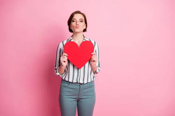 Retrato de positivo encantador menina tem 14-fevereiro data enviar beijos de ar para seu namorado ela começa vermelho grande cartão de papel coração desgaste cinza elegante calças isoladas sobre cor rosa fundo — Fotografia de Stock