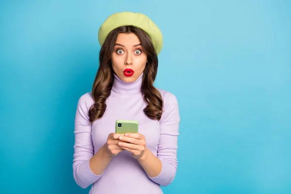 Портрет дивовижної дівчини використовує мобільний телефон, читає інформацію про соціальну мережу, вражений погляд дурний одяг бузкового кольору, одяг джемпер ізольований на фоні синього кольору — стокове фото