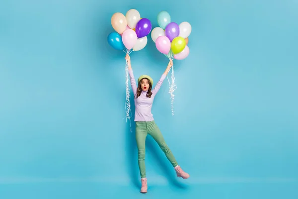 Full size foto van gekke mooie dame houden veel luchtballonnen armen opheffen wind blazen slijtage paarse jumper baret cap groene broek laarzen geïsoleerde blauwe kleur achtergrond — Stockfoto