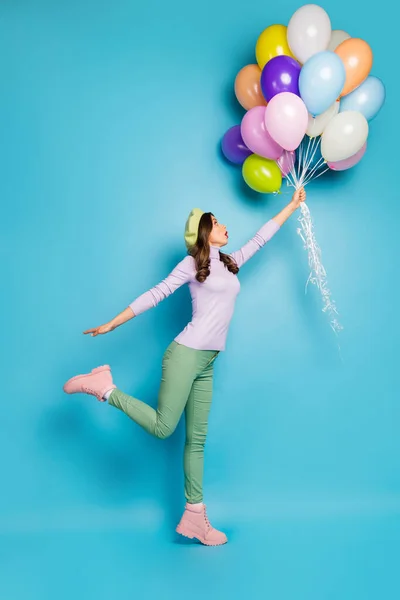 Longitud completa foto vertical de la señora loca boca abierta celebrar muchos globos de aire levantándose con el viento desgaste púrpura suéter boina gorra pantalones verdes botas aisladas de color azul de fondo — Foto de Stock