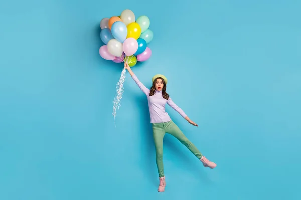 Ich glaube, ich kann fliegen. Ganzkörperfoto der hübschen Dame halten bunte Luftballons schockiert Aufstehen mit Wind tragen lila Pullover Baskenmütze grüne Hose Schuhe isoliert blaue Farbe Hintergrund — Stockfoto