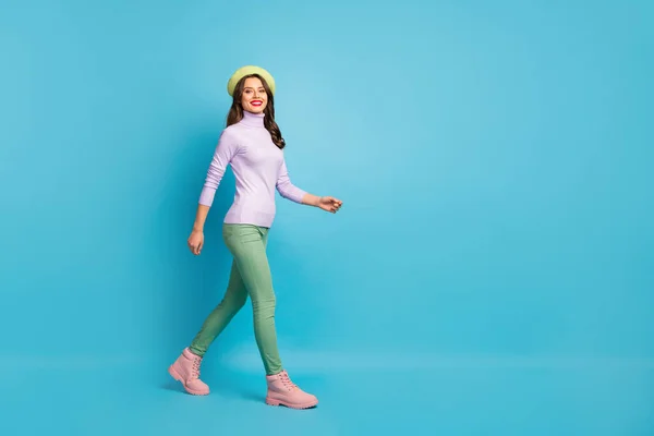 Ganzes Profilfoto von hübschen Touristin zu Fuß Straße im Ausland Reisende tragen grüne Baskenmütze lila Rollkragenpullover Hose Stiefel isoliert blaue Farbe Hintergrund — Stockfoto