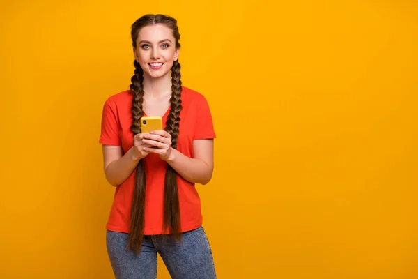 Foto de la señora bastante divertida sostenga las manos del teléfono trenzas largas blogger millennial buen humor persona creativa desgaste casual camiseta roja jeans aislados de color amarillo brillante fondo — Foto de Stock