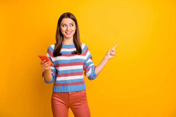 Retrato del promotor positivo alegre de la muchacha utilice el copyspace del dedo del índice del punto del teléfono elegante indica los anuncios que la promoción lleva pantalones del suéter aislados sobre fondo brillante del color del brillo —  Fotos de Stock