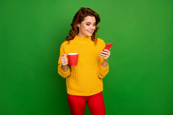 Retrato de la mujer alegre positivo descanso relajarse usar smartphone leer noticias de la red social celebrar la taza de bebida caliente desgaste de punto pantalones de suéter acogedor aislado sobre brillante brillo color fondo — Foto de Stock