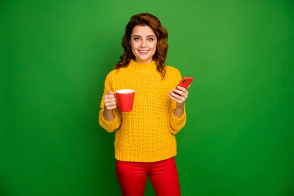 Positieve vrolijke vrouw rust ontspannen hold mok met cacao drank gebruik slimme telefoon genieten van social media nieuws dragen gebreide trui broek geïsoleerd over heldere glans kleur achtergrond — Stockfoto