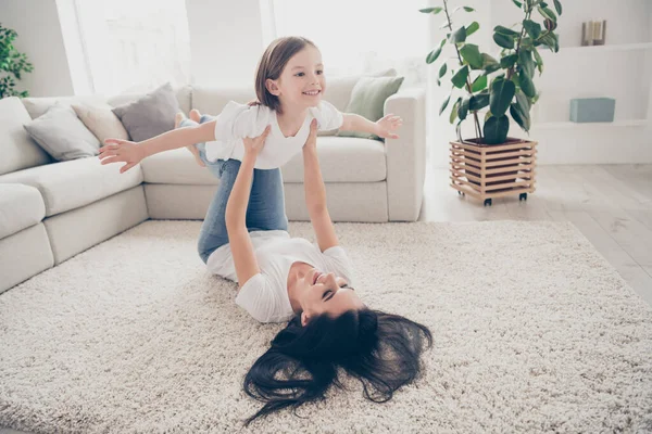 Full body foto di dolce carino idilliaca mamma il suo bambino si tiene per mano immaginare aereo volare cielo laici tappeto indossare bianco t-shirt jeans denim a piedi nudi in camera al chiuso — Foto Stock