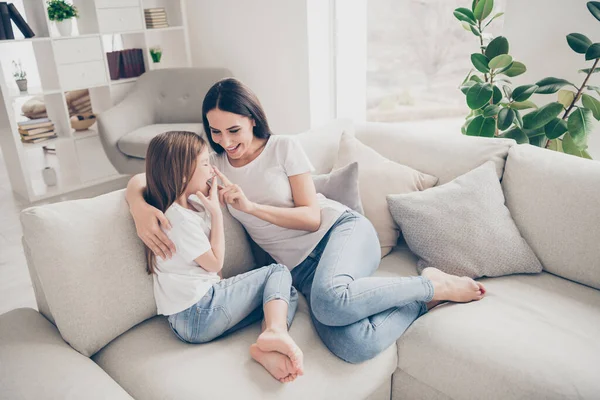 Фото красивой маленькой девочки очаровательной мамочки, обнимающейся с удовольствием, играющей на сенсорном носу, смеющейся сидя на удобном диване и проводя выходные вместе в закрытом доме — стоковое фото