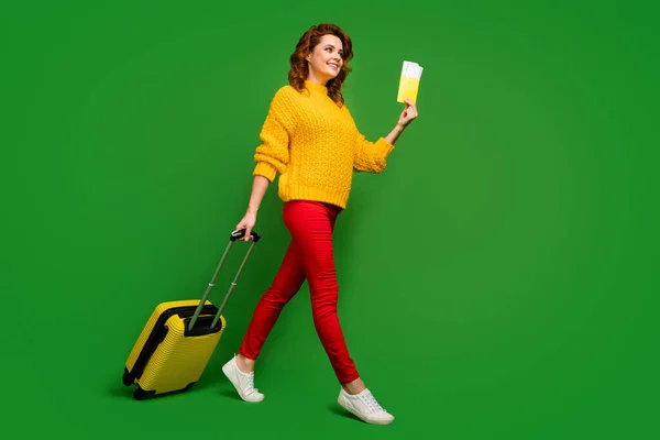 Foto de perfil de tamaño completo de la señora alegre celebrar boletos pasaporte viaje al extranjero caso de balanceo ir tabla de registro de vuelo desgaste suéter amarillo pantalones rojos zapatos aislados de color verde fondo —  Fotos de Stock