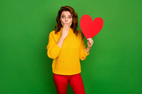 Foto de senhora animado segurar papel forma de coração cartão postal esconder boca não acredito bonito cara convidou sua data usar amarelo malha camisola vermelho calças isoladas cor verde fundo — Fotografia de Stock