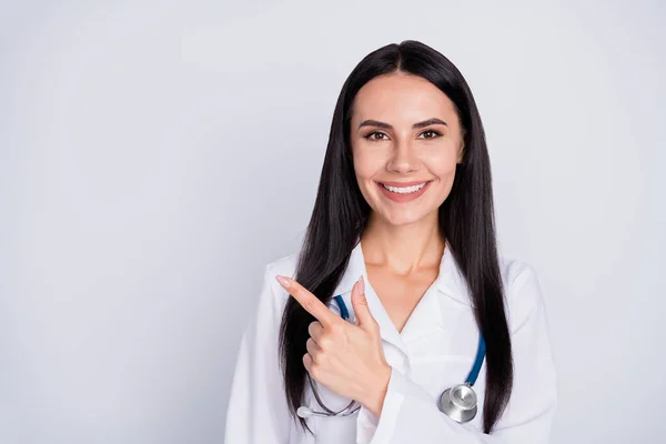 Photo of attractive doctor practitioner lady good mood smiling to patients direct finger empty space good insurance offer wear white lab coat stethoscope isolated grey color background — Stock Photo, Image