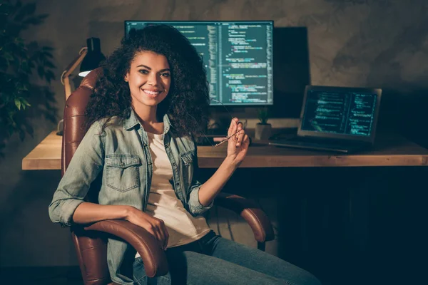 Portret van positief geschoolde afro-Amerikaanse meisje web designer ingenieur zitten stoel genieten van haar nacht bedrijfsgegevens werk houden bril in werkplek werkstation — Stockfoto