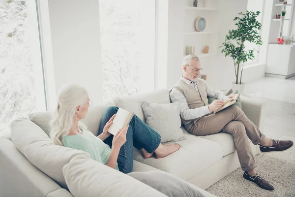 Felül szög fotó szép házastársak olvasni nyomtatott fikció könyv öltözött farmer teal barna pulóverek szemüveg ül díván a szobában — Stock Fotó
