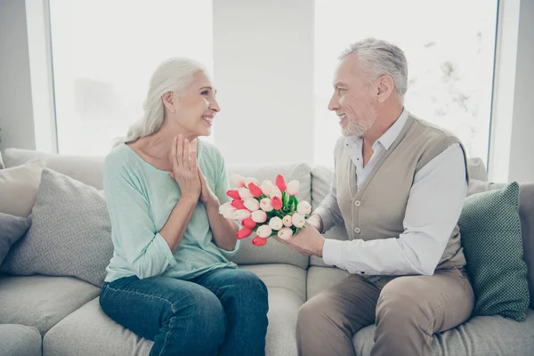 Perfil foto de romance momento envelhecido par aniversário feriado dando grande vermelho tulipas monte sentado sofá — Fotografia de Stock