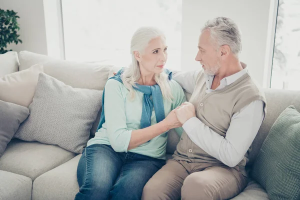 Фото двох красивих літніх людей, які тримають руки, емоційно виглядають очима, сидячи затишним диваном у приміщенні — стокове фото