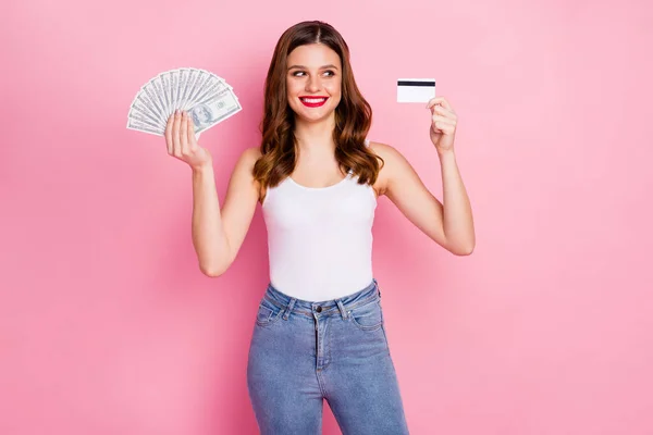 Portrait de fille freelance joyeux positif tenir de l'argent fan de carte de débit regarder profiter des économies de jackpot de loterie porter jeans en denim singulet blanc isolé sur fond de couleur rose — Photo