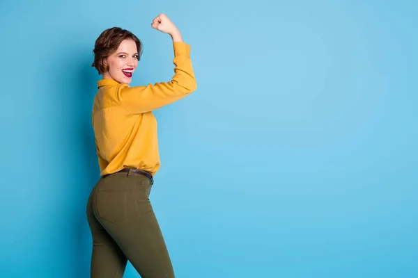 Profilfoto der hübschen Dame halten heben Bizeps Handarm zeigen perfekte Bizeps-Gymnastiktraining starke starke Frau tragen gelbes Hemd grüne Hose isoliert helle blaue Farbe Hintergrund — Stockfoto