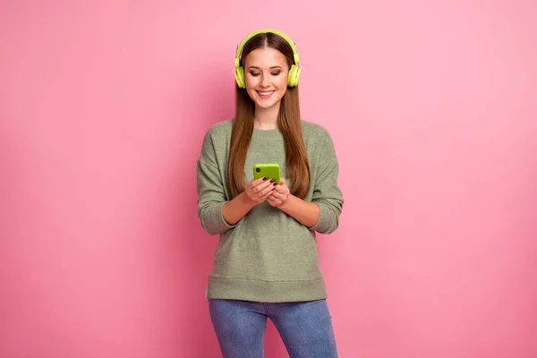 Портрет позитивної веселої дівчини використовує мобільний телефон мають навушники слухати музику в її списку відтворення насолоджуйтесь холодним носінням гарний светр ізольований на пастельному кольоровому фоні — стокове фото