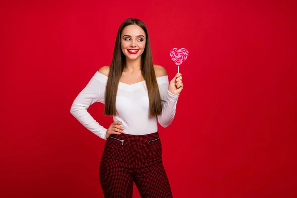 Retrato de positivo alegre menina segurar saboroso doce coração forma lolipop olhar quer comer desgaste elegante tendência beleza roupa branca isolado sobre brilhante brilho cor fundo — Fotografia de Stock