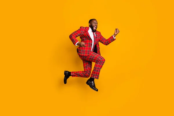 Full body profile photo of crazy dark skin guy jump high up celebrate achievement scream loud wear plaid red costume blazer pants shoes isolated bright yellow color background — Stock fotografie