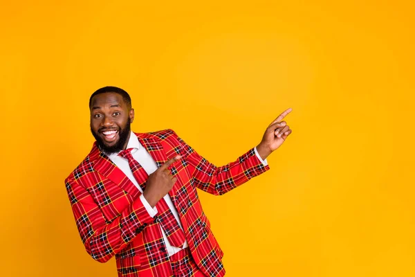 Photo of funny sales person dark skin guy indicating fingers side empty space advising novelty product wear plaid costume blazer shirt tie pants isolated yellow color background