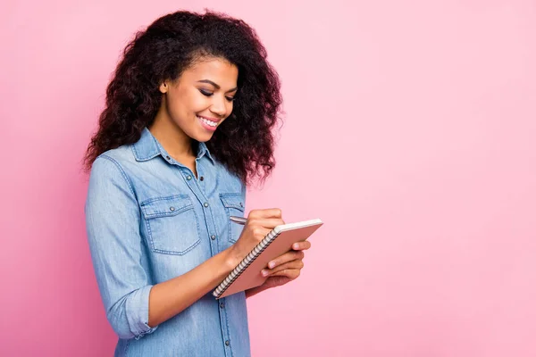 Portrait of positive focused afro american girl college student write copy book university lecture wear casual style denim shirt isolated over pink color background — Stock Photo, Image